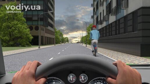 Велосипедист на дорозі попереду автомобіля, вид з місця водія, руки на кермі та панель приладів, міська вулиця з будинками та деревами.