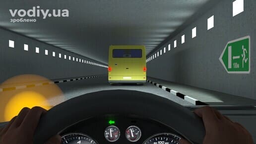 Рух автомобіля в тунелі за автобусом, увімкнений лівий покажчик повороту на панелі приладів, дорожній знак 5.80.1.