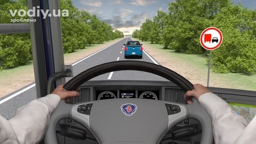 Вид з кабіни вантажівки на синій автомобіль попереду, дорожній знак 3.27 «Обгін вантажним автомобілям заборонено» праворуч біля дороги.