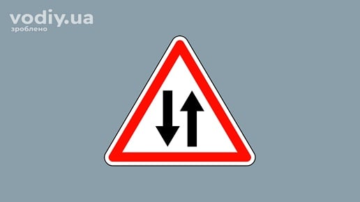 Дорожній знак 1.26 «Двосторонній рух» на сірому фоні. Попередження про початок ділянки дороги із зустрічним рухом після одностороннього.