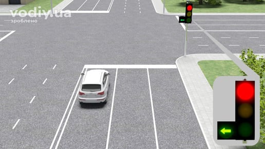 Білий автомобіль у лівій смузі перед перехрестям, червоний сигнал світлофора та зелена стрілка у додатковій секції ліворуч.