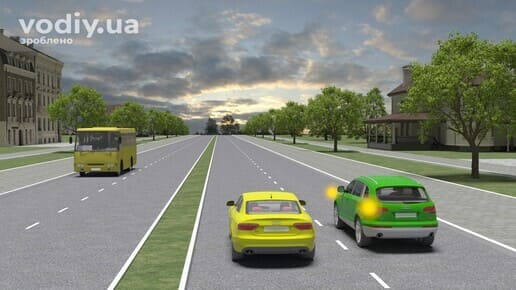 Зелений автомобіль з увімкненим лівим покажчиком повороту та жовтий автомобіль рухаються попутно по дорозі з розділювальною смугою.