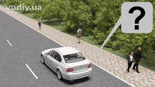 Білий автомобіль на дорозі поруч із пішохідною доріжкою з бруківки, пішоходи йдуть по тротуару вздовж проїзної частини.