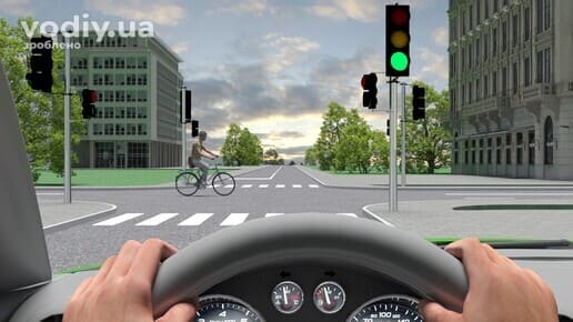 Велосипедист перетинає перехрестя, зелений сигнал світлофора, вид з місця водія автомобіля.