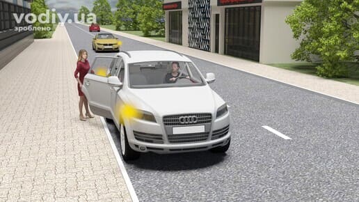 Пасажирка відчиняє двері білого автомобіля під час руху, увімкнені фари, край проїзної частини та тротуар.