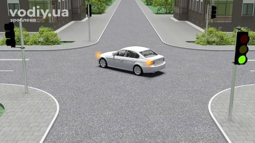 Білий автомобіль повертає на перехресті з увімкненим правим покажчиком повороту, зелений сигнал світлофора.
