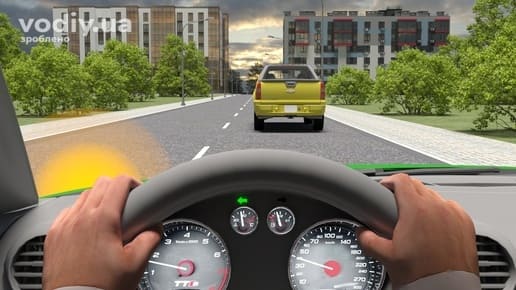 Вид з місця водія, руки на кермі, увімкнений лівий покажчик повороту, жовтий пікап попереду на дорозі в населеному пункті.