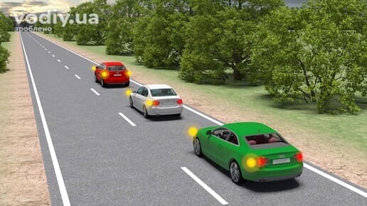 Зелений, білий та червоний автомобілі на дорозі поза населеним пунктом, увімкнені ліві покажчики повороту у всіх транспортних засобів.