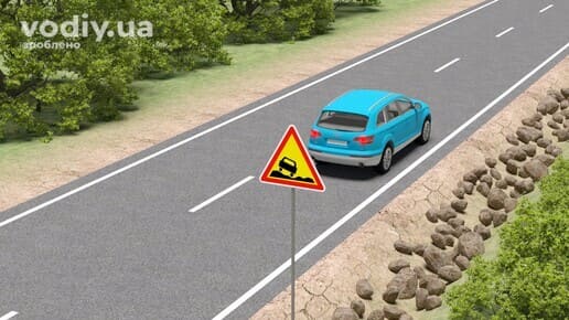 Дорожній знак 1.15 «Небезпечне узбіччя», блакитний автомобіль на дорозі поза населеним пунктом, каміння на узбіччі та край проїзної частини.