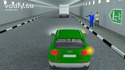 Зелений автомобіль з увімкненим правим покажчиком повороту в тунелі, пасажири на тротуарі біля знака 5.80.1, попереду вантажівка.