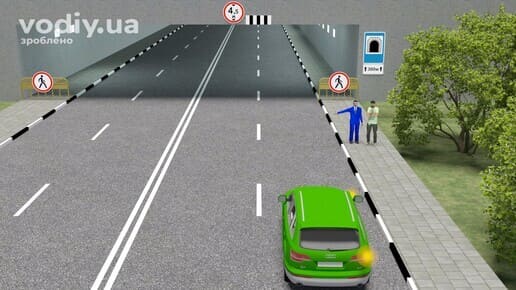 Зелений автомобіль з увімкненим покажчиком повороту перед в'їздом у тунель, дорожні знаки: 3.9, 3.18, 5.74, 7.1.1, чорно-білий бордюр.