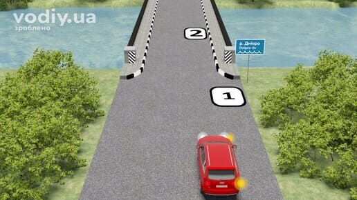 Червоний автомобіль на дорозі перед мостом через річку, дорожній знак 5.65.1 «Назва об’єкта», місця для зупинки позначені цифрами 1 та 2.