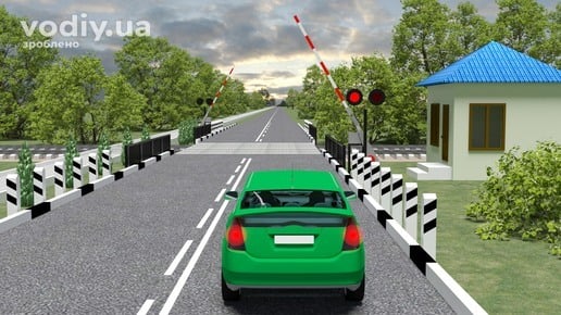 Зелений автомобіль перед залізничним переїздом, увімкнений червоний сигнал світлофора, відкриті шлагбауми та стовпчики з розміткою 2.4.