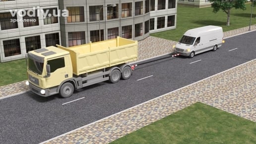 Буксирування вантажним автомобілем білого мікроавтобуса на жорсткому зчепленні по міській дорозі.