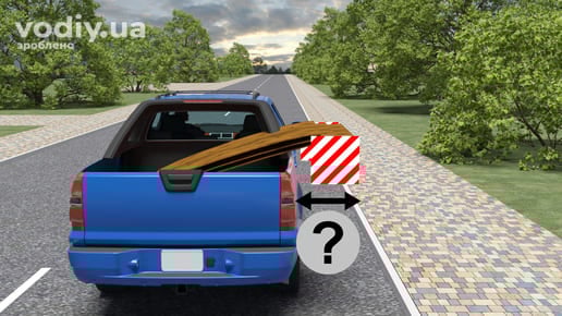 Синій пікап перевозить вантаж, що виступає за ширину кузова та позначений сигнальним щитком, вимірювання відстані від габаритного ліхтаря.